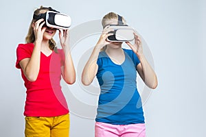 Virtual Reality Simulation. Pair of Caucasian Twin Girls Playing With VR Virtual Reality Helmets Together Indoors