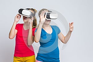 Virtual Reality Simulation. Pair of Caucasian Twin Girls Playing With VR Virtual Reality Helmets Together Indoors