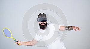 Virtual sport concept. Man with beard in VR glasses beating pitch, grey background. Guy with VR glasses play tennis with