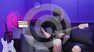 Virtuoso guitarist playing an electric guitar on sofa with color LED lights At Home Studio. Man plays the electric