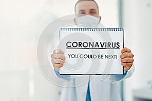 This virus doesnt discriminate. a scientist holding a sign with CORONAVIRUS-YOU COULD BE NEXT on it in a laboratory.