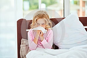 Virus infection. Little girl with runny nose suffering from cold or flu while lying in bed at home