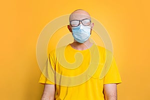 Virus protection. Against a yellow background stands a bald man in a yellow t-shirt, fogging glasses and a medical mask. Concept