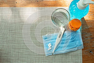 Virus protection concept, glass of water protective face-mask, orange bottle of pills and alcohol gel and thermometer are on a