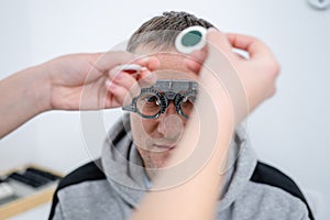 Vision correction. Selection of eyeglasses. Professional trial frames on male patient face while doctor checks eyesight