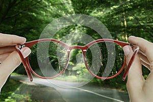 Vision correction. Woman looking through glasses and seeing forest clearer