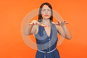 Vision problems. Disoriented young brunette woman in denim dress standing with closed eyes and outstretched hands
