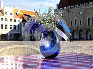 Tallinn Estonia blue  vase  with flowers  and Estonia flag  symbols  on street cafe table top  old town  castle hall square panora photo