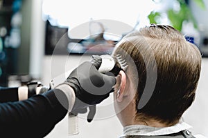 Visit to the barbershop. Hairdresser, barber shaves client`s temples,sides with hair clipper. Young stylish man makes fashionable