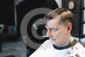 Visit to the barbershop. Hairdresser, barber shaves client`s temples,sides with hair clipper. Young stylish man makes fashionable