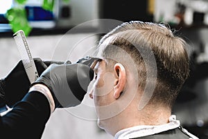 Visit to the barbershop. Hairdresser, barber shaves client`s temples,sides with hair clipper. Young stylish man makes fashionable