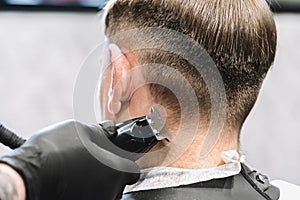 Visit to the barbershop. Hairdresser, barber shaves client`s temples,sides with hair clipper. Young stylish man makes fashionable