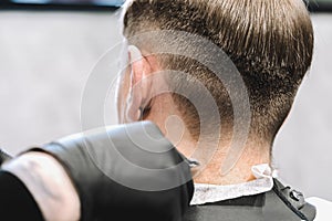 Visit to the barbershop. Hairdresser, barber shaves client`s temples,sides with hair clipper. Young stylish man makes fashionable