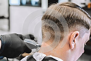 Visit to the barbershop. Hairdresser, barber shaves client`s temples,sides with hair clipper. Young stylish man makes fashionable