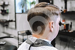 Visit to the barbershop. Hairdresser, barber shaves client`s temples,sides with hair clipper. Young stylish man makes fashionable