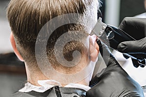 Visit to the barbershop. Hairdresser, barber shaves client`s temples,sides with hair clipper. Young stylish man makes fashionable