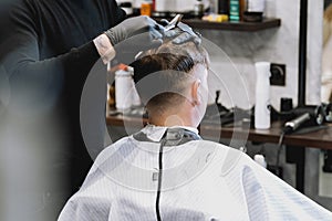 Visit to barbershop. Stylish man makes fashionable haircut. Barber, hairdresser, stylist with scissors, comb cutting,combing hair