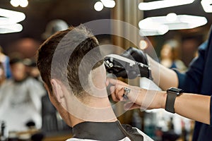 Visiting barbershop. Close up shot of professional barber working with hair clipper, making trendy haircut for client