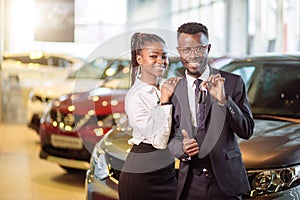 Visiting car dealership. couple holding key of their new car, looking at camera