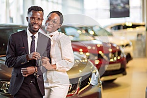 Visiting car dealership. couple holding key of their new car, looking at camera