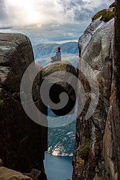 Visiting Norway Kjeragbolten located south of Lysefjorden Young woman sits on top of gian boulder in meditative pose