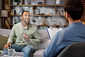 Visiting a psychologist A man sits on a couch and talks to a psychotherapist. He thanks the doctor and smiles, therapy