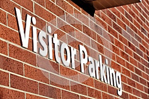 A visitor parking sign on a red brick wall