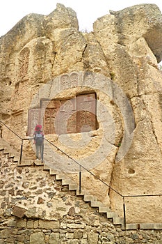 Visitor on the Staircase Impressed by Group of Khachkar or Armenian Cross-stones on the Cliff Wall, Geghard Monastery Complex