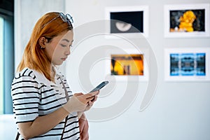 Visitor woman standing takes picture art gallery collection in front framed paintings pictures
