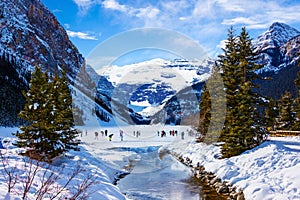 Visitors skating on frozen Lake Louise in Winter against the backdrop of the stunning Victoria Glacier