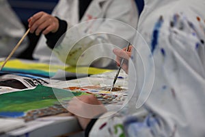 Visual art students painting close up and wearing aprons or art smocks