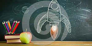 Visual arts on a blackboard books, apples, pencils, rocket drawing