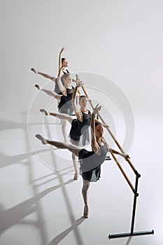 Visual harmony. Top view on four teen girls, ballerinas in black costumes standing at barre and practicing against grey