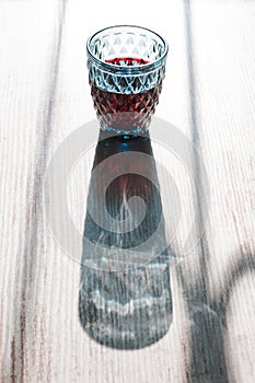 Visual optical illusion with light and shadows play of harsh sunlight shining through a blue crystal red wine glass