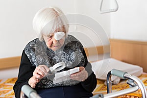 Visually impaired elderly 95 years old woman sitting at the bad trying to read with magnifying glass. photo