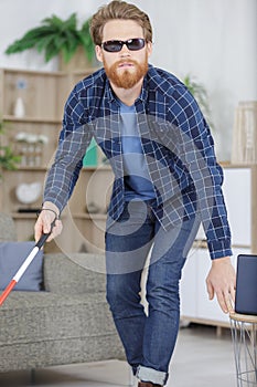 visually impaired man using stick to move around home