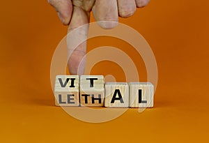 Vital vs lethal symbol. Businessman turns wooden cubes and changes the word `lethal` to `vital`. Beautiful orange background,