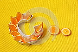Vitamin C or Ascorbic acid nutrient in food concept. Plate in shape of letter C with orange slices on bright yellow background
