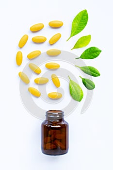 Vitamin C bottle and pills with  green leaves on white