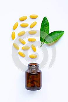 Vitamin C bottle and pills with  green leaves on white