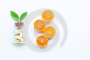 Vitamin C bottle and pills with orange fruit on white