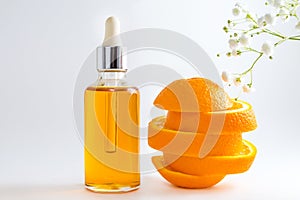 Vitamin C serum in cosmetic bottle with dropper, sliced orange and flowers on white background. Organic SPA cosmetics with herbal