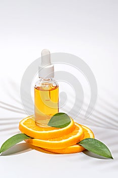 Vitamin C serum in cosmetic bottle with dropper, sliced orange and green leaves on white background. Organic SPA