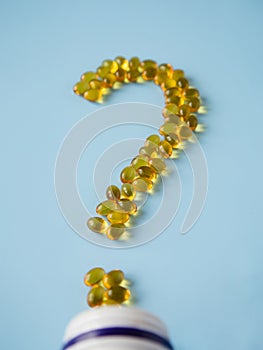 Vitamin capsules on a blue surface in the form of a question mark. Omega-3 and Vitamin D. Nutritional supplements. Yellow pills.