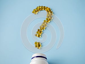 Vitamin capsules on a blue surface in the form of a question mark. Omega-3 and Vitamin D. Nutritional supplements. Yellow pills.