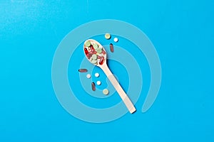 Vitamin capsules in a wooden spoon on a colored background. Pills served as a healthy meal. Drugs, pharmacy, medicine or