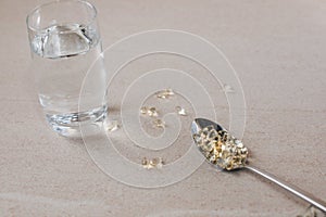 Vitamin D 3 capsules in a spoon on a stone beige table and a glass of water