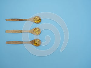 Vitamin D, E or fish oil capsules in wooden spoons on blue background with copy space, top view, flat lay