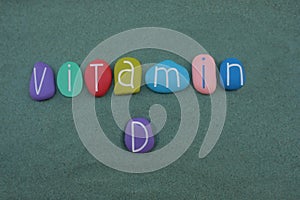 Vitamin D text composed with multi colored stone letters over green sand