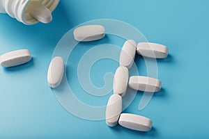 Vitamin E pills fell out of a white jar on a blue background. The letter E is an inscription